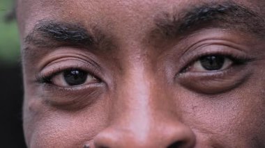 Siyah adamın gözlerinin, geniş bir gülümseme ve neşeli bir ifadeyle kameraya bakışıyla kendine güveni ve özgüveni gösteren yakın çekimi.