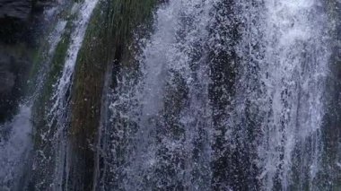 Düşen su akıntıları, ıslak yosun ve taşın üzerinden yüksek hızlı kamerayla çekilen çok yavaş çekimde akıyor.