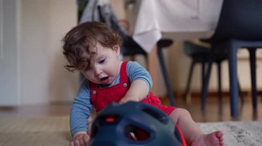 Yeni yürümeye başlayan bir çocuk, kaska dokunmak ve keşfetmek için öne doğru eğilir. Nazik bir merakla şeklini inceler ve erken öğrenmenin huzurlu bir anını oluşturur ve dikkatini toplar.