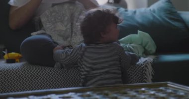 Bebek, oturma odasındaki kanepede kameraya bakmadan sakin ve samimi bir aile anı yaratarak, ellerini tutarak oturan bir yetişkinin karşısında dinleniyor.