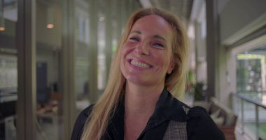 Kameraya hafifçe gülümseyen bir kadın, koridorda dururken kibarlık, profesyonellik ve kendine güven yansıtıyor.