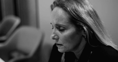 Kapalı gözlü, gergin yüzlü, kurumsal tükenme anında derin duygusal stres hisseden orta yaşlı bir kadın. Siyah ve beyaz.