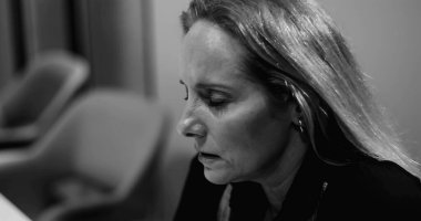 Kapalı gözlü, gergin yüzlü, kurumsal tükenme anında derin duygusal stres hisseden orta yaşlı bir kadın. Siyah ve beyaz.