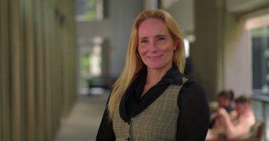 Modern bir şirket ortamında geniş ofis koridorlarında gülümseyen kendine güvenen bir iş kadını.