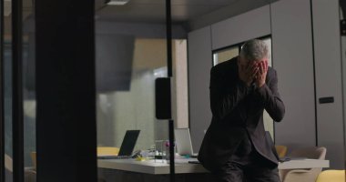 Şirket yöneticisi, sessiz bir ofiste tek başına otururken yüzünü ellerle kapatarak duygulara boğuldu.