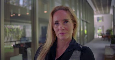 Modern koridorda kendine güvenen bir ifadeyle kameraya bakan bir kadın, azim ve profesyonelliği yansıtıyor.