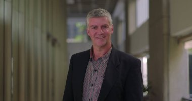 Ofis salonunda yavaşça gülümseyen, sakin ve düşünceli orta yaşlı bir adamın yakın çekimi.