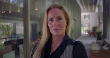 Modern koridorda kendine güvenen bir ifadeyle kameraya bakan bir kadın, azim ve profesyonelliği yansıtıyor.