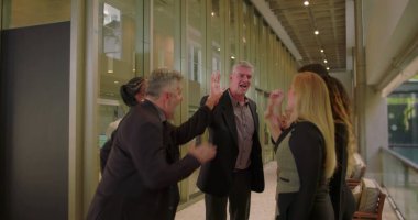 Neşeli iş grubu kapalı alanda beşlik çakıyor, iş arkadaşları takım başarısını ve işbirliği içindeki profesyonel atmosferde birlik olduğunu kabul ediyor