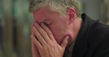 Orta yaşlı bir adamın yüzünü iki eliyle ofis odasında kapatması duygusal bunalımı ya da sessiz çalışma ortamında sıkıntıyı ifade etmesi.