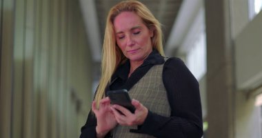 Ofis koridorunda telefonu komik bir ifadeyle kullanan iş kadını ara verdiğinde mesajları karıştırıyor.