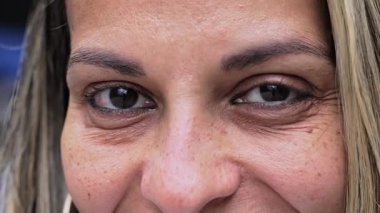 Kahverengi gözlü, gülümseyen sarışın kadın göz kalemiyle kameraya göz alıcı ve etkileyici bir şekilde bakıyor.