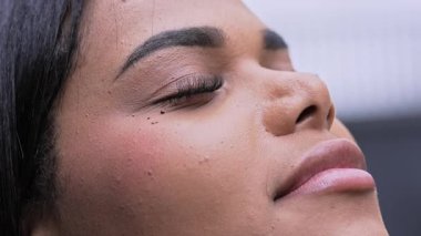 İfade dolu bakışları ve başı yukarı eğilmiş genç bir kadın yavaşça gözlerini açar ve geniş bir gülümseme ve hoşnutlukla yukarıya bakar.