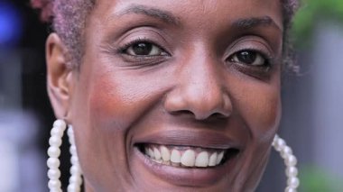 Yakından bakınca gülümseyen siyah kadın. Küpe takıyor ve neşeli bir şekilde kameraya bakıyor. Ve arka planı bulanık.