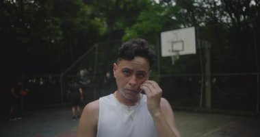 Basketbol formalı genç adam saha üstüne sahada duruyor, kameraya ciddi bir ifadeyle bakıyor, yoğunluğu ve atletik odağı yakalıyor.