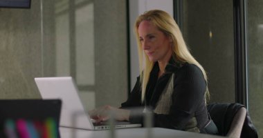 Profesyonel kadın, modern ofis toplantı odasında dizüstü bilgisayarla yazarken cam duvarlar ve iş sırasında çağdaş dekor kullanıyordu.