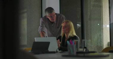 Erkek iş arkadaşı ekranı işaret ederken, sarışın iş kadını ofis toplantı odasında iş birliği yaparken dinliyor ve ilişki kuruyor.