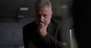 Olgun iş adamı, modern kurumsal ofis ortamında yoğun yönetim kurulu tartışması sırasında elini uzatarak düşünceye daldı.