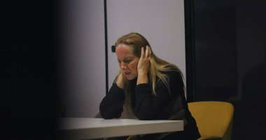 Yorgun orta yaşlı bir profesyonel modern ofisteki konferans masasında yalnız başına geçirdiği anlarda kulaklarını tıkar ve gözleri kapatır.