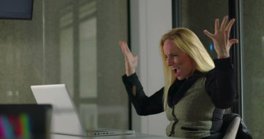 Modern ofis ortamındaki iş toplantısı sırasında dizüstü bilgisayara bakarken heyecanlı kadın yöneticiler tezahürat yapıyor ve başarıyı kutluyor. 