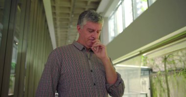 Orta yaşlı bir adam ofis koridorunda elleri ağızlarına yakın duruyor endişeli ifadeye bakıyor profesyonel settin 'deki endişe ve endişe dolu stresi iletiyor.