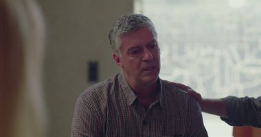 Terapi seansı sırasında, başka bir grup üyesi elini omzuna koyduğu zaman, gözleri aşağıda bir şekilde oturan bir adam, empati ve bağlantı anında destek alır. 