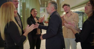 Ofis koridorundaki destekleyici meslektaşlarından alkış alırken gülümseyen müteşekkir erkek profesyonel, tanınma ve takdir anı 