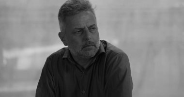 Grup terapisi sırasında çöken bir adam, acı içinde başını eğerken başka bir grup üyesi omzunda rahatlatıcı bir elle sessiz destek sunuyor, siyah ve beyaz. 