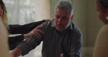 Adam grup terapisi sırasında duygusal olarak açılır. Savunmasızlığını belirtirken öne eğilir ve çemberde oturan şefkatli akranlarından destek alır. 