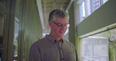 Ofis koridorunda cep telefonu kullanan orta yaşlı bir adam modern iş çevrelerinde mobil cihazlarla uğraşıyor.