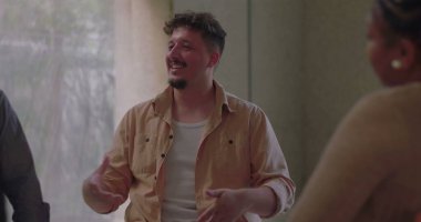 Terapi grubunda yürekten konuşan bir adam, özenli ve destekleyici katılımcılarla çevriliyken kişisel hikayelerini paylaşmak için anlamlı jestler kullanır. 