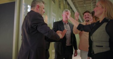 Çeşitli iş adamları ofis koridorunda beşlik çakıyor. Bir grup profesyonel modern iş yerinde başarıyı ve takım çalışmasını coşkulu bir jestle kutluyor.