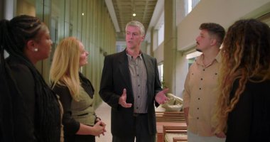 Ofis koridorunda yönetici konuşma ekibi, modern kurumsal ortamda iş yeri tartışması sırasında dinleyen çeşitli profesyoneller grubu.