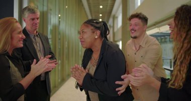 Çeşitli takımlar şirket koridorunda alkışlarken mutlu kadın gülümsüyor. Profesyoneller iş ortamında cesaret ve birlik gösteriyor.