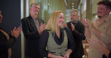 Ofis koridorundaki çeşitli iş arkadaşlarından alkış alan gülümseyen kadın, başarıyı kutlayan ve iş yerinde takdir gösteren bir grup profesyonel. 