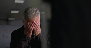 Stresli iş adamı, yüksek baskılı şirket toplantısı sırasında ofis konferans odasında tek başına dikilirken el ele vererek yüzünü kapatıyor.