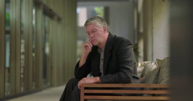 Orta yaşlı bir adam ofiste sessizce oturuyor, elleri çenesinde, düşünceli ve düşünceli görünüyor, barışçıl modern çalışma ortamında