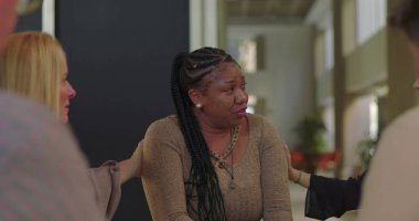 Duygusal terapi sırasında ağlayan kadın, güçlü bir hassasiyet anında destek ve şefkat sunan grup üyeleri tarafından teselli ediliyor.