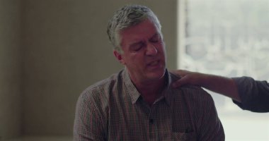 Terapi seansı sırasında, başka bir grup üyesi elini omzuna koyduğu zaman, gözleri aşağıda bir şekilde oturan bir adam, empati ve bağlantı anında destek alır.