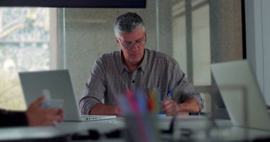 Odaklanmış orta yaşlı bir adam, ofis toplantısı sırasında dizüstü bilgisayardaki notları ve tipleri gözden geçirir.