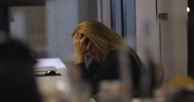 Hüsrana uğramış iş kadını elleri yüzü önünde oturmuş, ofis toplantısı talep ettikten sonra yoğun stresi yönetmeye çalışıyor.