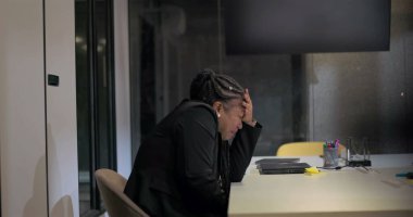 Kafası cam toplantı odasında olan Afrikalı Amerikalı bir şirket çalışanının uzaktan görünüşü duygusal yorgunluk, yorgunluk ve işyeri izolasyonunu resmediyor.