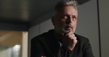 Düşünceli iş adamı, şirket toplantısında elleri çenesinde ve yoğun bakışlarıyla profesyonel kurul odasında kayboldu.