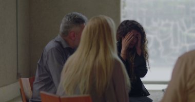 Sıkıntılı genç kadın grup terapisi sırasında acı dolu anılarını paylaştığı için ağlıyor, yaşıtları sessiz kalarak destek çemberinde şefkatli bir şekilde dinliyorlar.