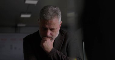 Olgun iş adamı, modern kurumsal ofis ortamında yoğun yönetim kurulu tartışması sırasında elini uzatarak düşünceye daldı.