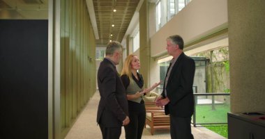 Modern ofis koridorunda konuşan bir grup iş arkadaşı, gayriresmi toplantı sırasında gevşek iş yeri sohbetine girişen profesyonel takım.