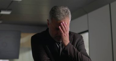 Stresli iş adamı, yüksek baskılı şirket toplantısı sırasında ofis konferans odasında tek başına dikilirken el ele vererek yüzünü kapatıyor.