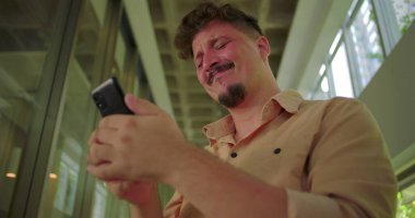 Telefonu acılı bir gülümsemeyle tutan, modern koridorda duygusal mesajlarla boğuşan, pişmanlık, hayal kırıklığı ya da evde duygusal hassasiyet duyan bir adam.