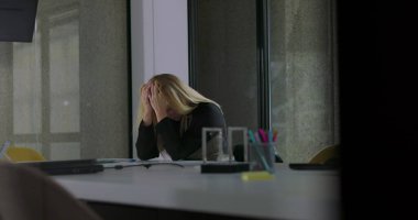 Kadın, modern ofiste masa başında otururken yüzünü iki eliyle kapatıyor. Sessiz bir şirket ortamında stres ya da duygusal hayal kırıklığını ifade ediyor.