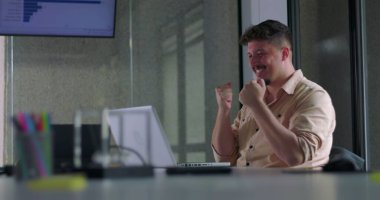 Erkek çalışan, ofiste dizüstü bilgisayarla çalışırken iki eliyle alkışlıyor.